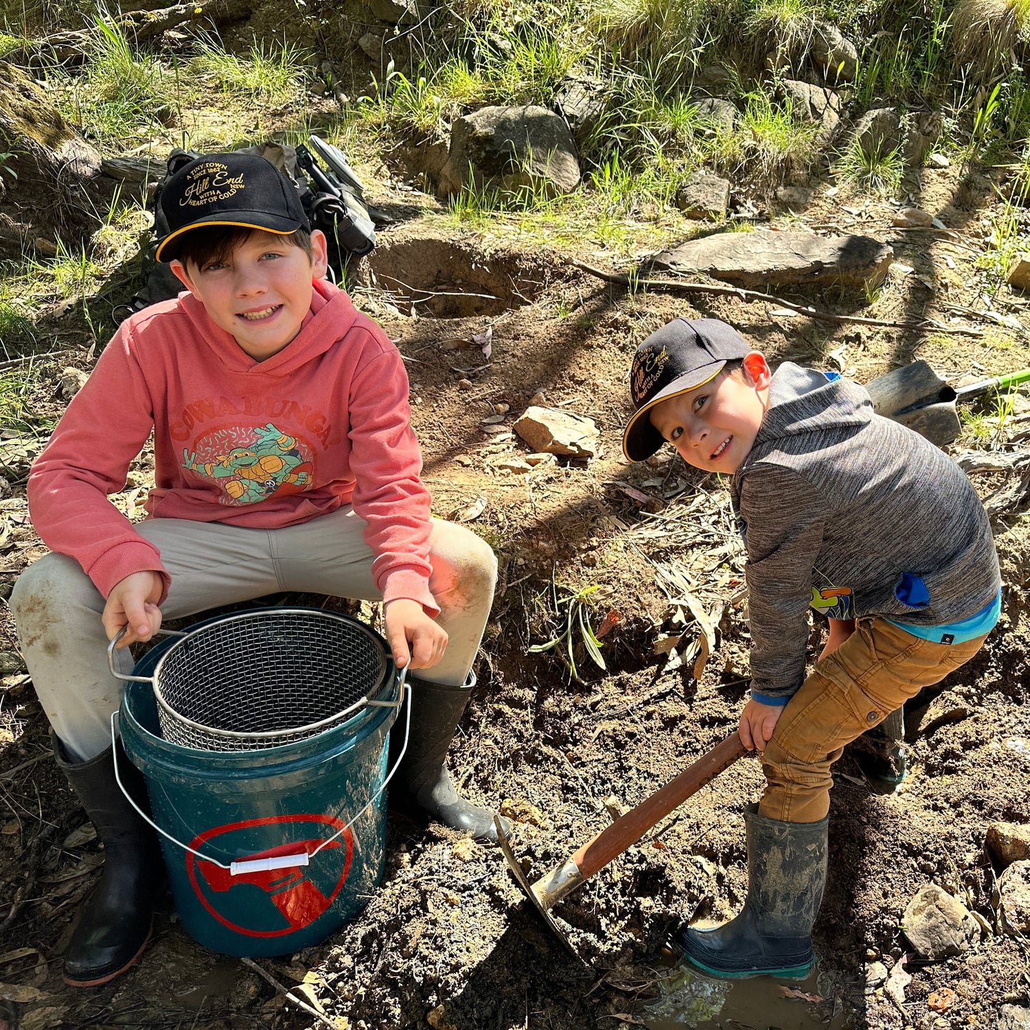 Two children in a natural setting with buckets and tools, likely involved in an outdoor activity.